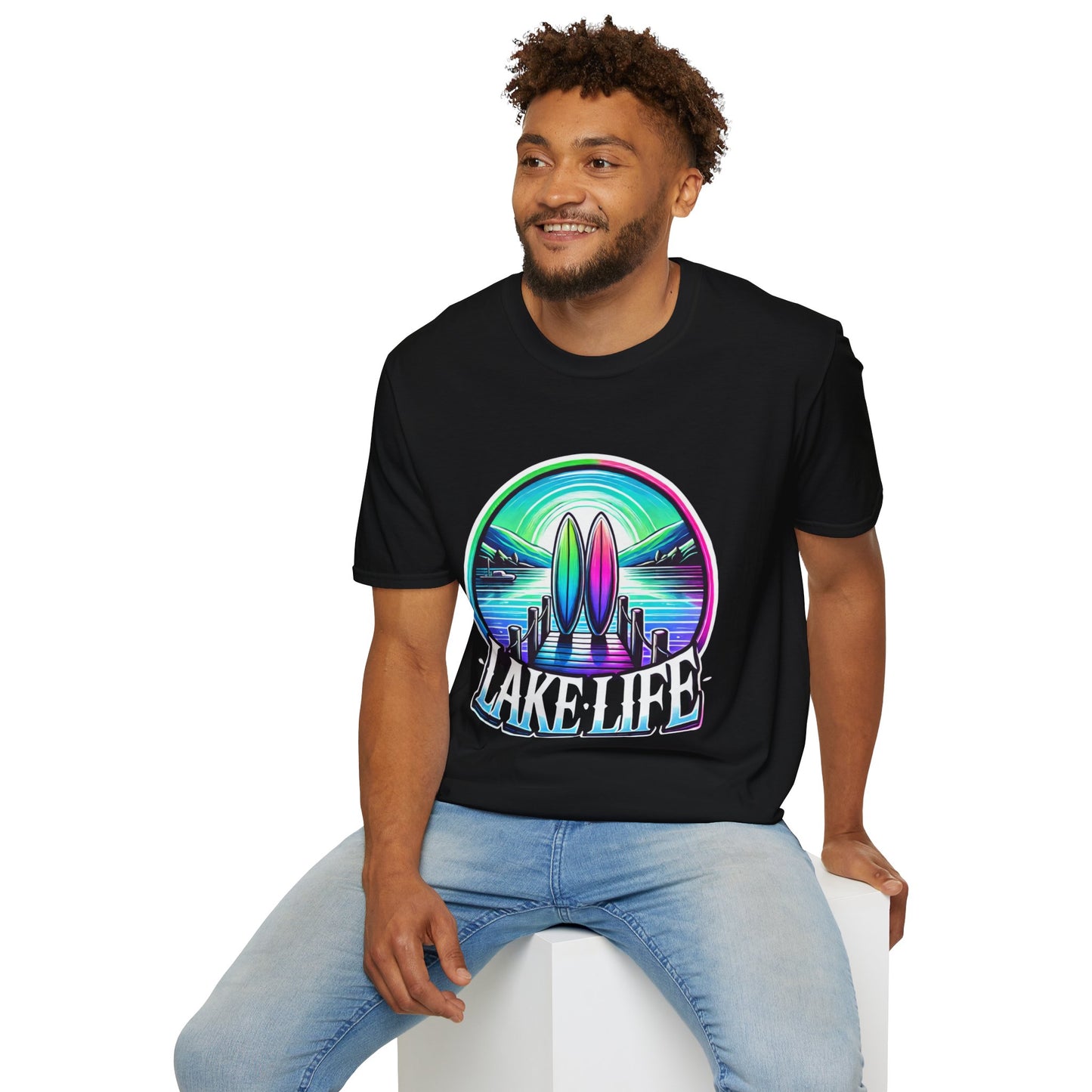 Man wearing black graphic tee with graphic design of a lake, surf boards, and a dock in vibrant colors